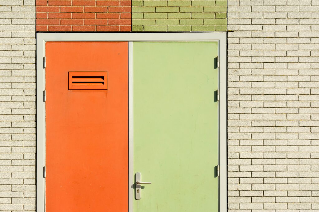 Orange and green door on a brick wall with modern design and security features.