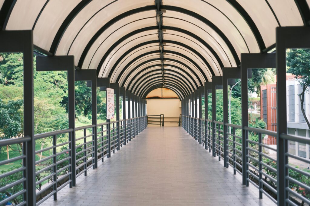 A long covered pedestrian bridge with metal railings, surrounded by greenery.